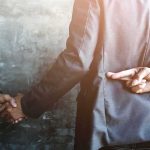 870,000 Suspected Of FRAUD — The Checks Cleared Five Years Ago businessperson shakes hands while crossing fingers behind back