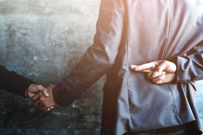 shutterstock_1007250361 businessperson shakes hands while crossing fingers behind back