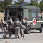 Soldiers carry a wounded comrade on a stretcher to a military ambulance