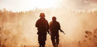 Iran INJURED Our Troops Weeks Ago — Nobody Told YOU Two soldiers walking through a smoky field at sunset