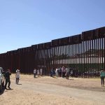Border fence with group of people and a patrol vehicle