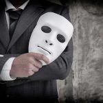 He Faked Military Service For $124K — Then Faked Something WORSE person in suit holding a white expressionless mask