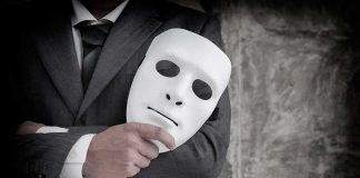 He Faked Military Service For $124K — Then Faked Something WORSE person in suit holding a white expressionless mask