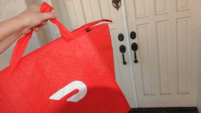 shutterstock_1607669812 Hand holding red insulated delivery bag at a front door