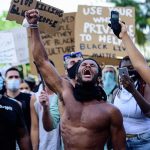 Netflix Roast Sparks Outrage: BLM DEMANDS Apology Shirtless protester raises fist while crowd holds signs