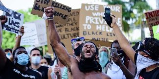 Shirtless protester raises fist while crowd holds signs