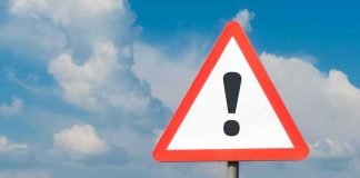 Warning road sign with exclamation mark against blue sky
