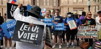 Christian Jones sits with a 'Let Us Vote' sign facing a crowd at a voting rights rally