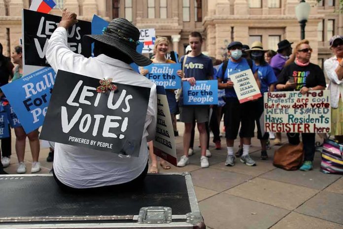Christian Jones sits with a 'Let Us Vote' sign facing a crowd at a voting rights rally