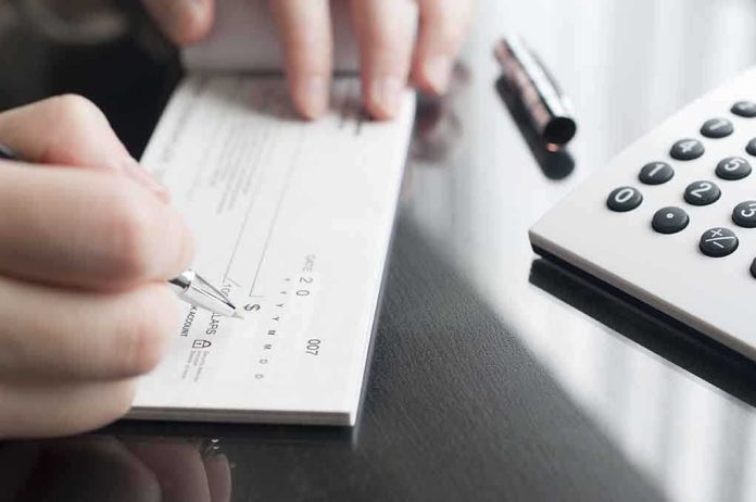 Person writing a check on a reflective surface with a calculator nearby