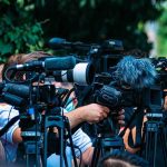 Medicare Freeze Sparks Outrage: Hidden Agenda? TV news cameras crowding together at an outdoor event