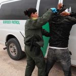 Border patrol agent detains a person against a van