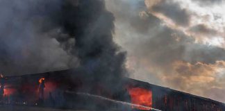 Firefighter on ladder spraying water at warehouse fire