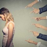 Young woman looking down while multiple hands point at her