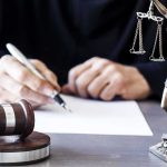 The DA Told His Staff To ‘Protect The Office’ — Now HE Needs Protecting Judge writing at desk with gavel and Lady Justice statue