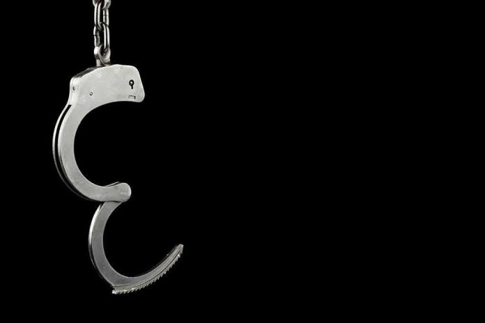 Open metal handcuff hanging against a black background