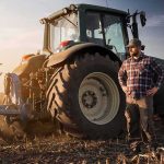 Farmer standing beside a tractor in a plowed field