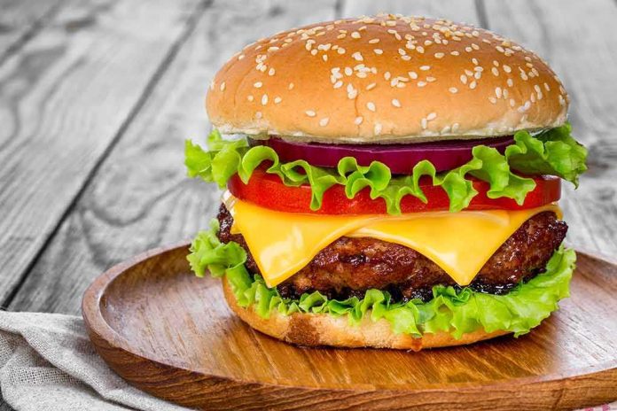 shutterstock_1053796058 Cheeseburger with lettuce, tomato, and onion on a wooden plate