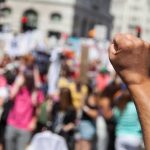 Democrat Hopeful’s VILE Name For His OWN Government Raised fist in foreground at a crowded street protest