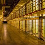 Prison cell block corridor with barred cells and upper walkways