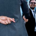 Businessman crosses fingers behind back during handshake