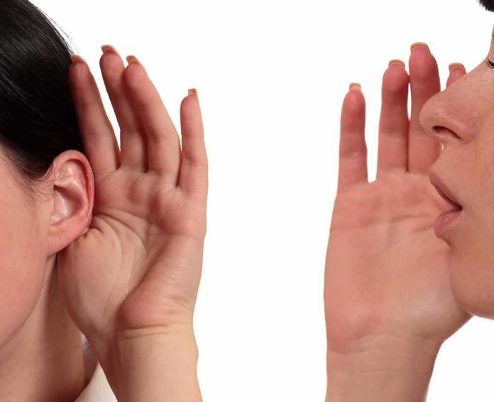 shutterstock_135276407 person whispering into another person's ear
