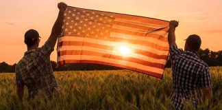Two people hold an American flag in a field at sunset