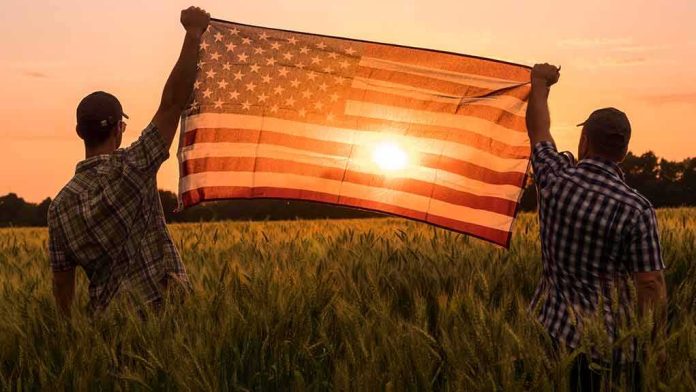 shutterstock_1432646948 Two people hold an American flag in a field at sunset