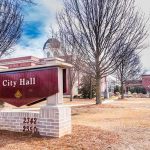 Democrat Mayor ACCUSED Of Scandalous Behavior City Hall sign in front of a red-brick municipal building