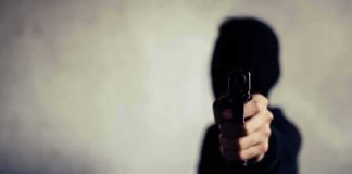 person in a hoodie pointing a handgun toward the camera