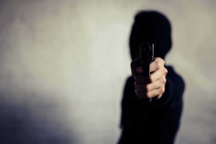 shutterstock_1681294804 person in a hoodie pointing a handgun toward the camera