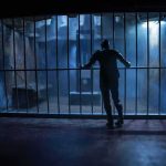 Silhouette of a person gripping prison cell bars