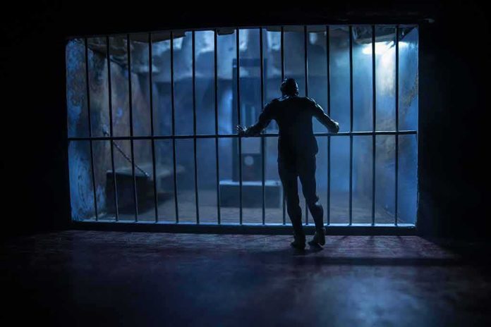 shutterstock_1917645122 Silhouette of a person gripping prison cell bars