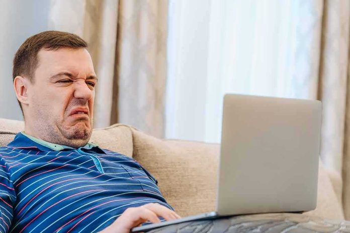 shutterstock_2121979469 Man grimacing while using a laptop on a couch