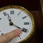 Trump Wants The Clock Change GONE — ONE Republican Is In The Way Hand adjusts the minute hand on a brass-rimmed clock with Roman numerals