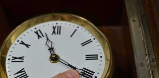 Trump Wants The Clock Change GONE — ONE Republican Is In The Way Hand adjusts the minute hand on a brass-rimmed clock with Roman numerals