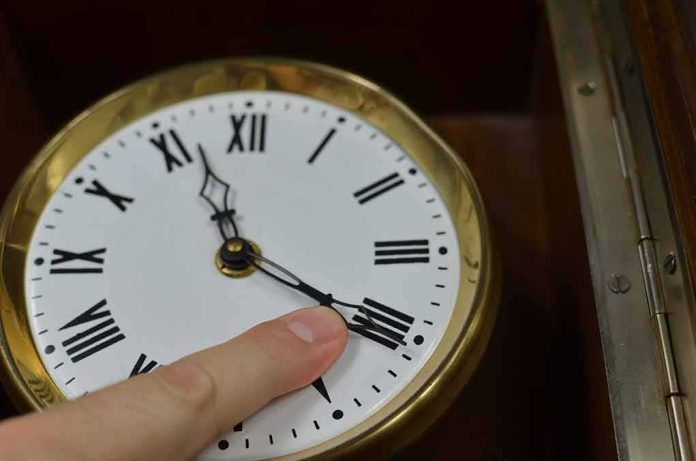 Hand adjusts the minute hand on a brass-rimmed clock with Roman numerals